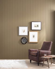 a brown chair sitting next to a wooden table in front of a wall with pictures on it