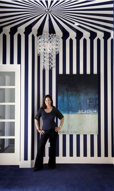 a woman standing in front of a blue and white striped wall with a chandelier