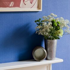 a vase with flowers sitting on a shelf next to a blue wall and framed photograph