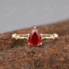 a close up view of a ring with a red stone in the center on top of a rock