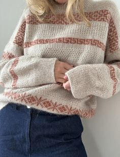 a woman wearing a sweater and jeans is posing for the camera with her hands on her hips