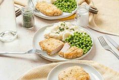 two plates with meat, peas and mashed potatoes on them next to silverware