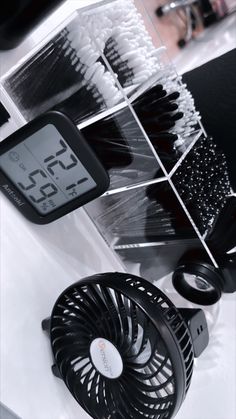 an alarm clock and fan sitting on top of a white table next to each other