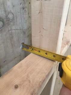 a person measuring the width of a piece of wood with a yellow tape measure ruler