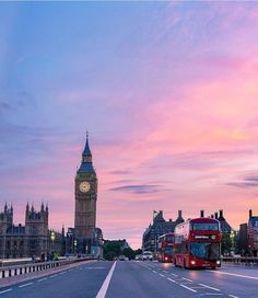 two red double decker buses driving down the street in front of big ben at sunset