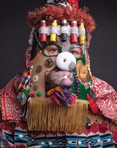 a man wearing an elaborate mask and headdress with buttons on his face, in front of a black background