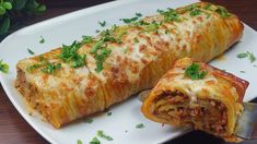 a white plate topped with an enchilada covered in meat and cheese next to a knife