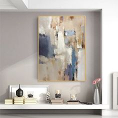 an abstract painting hangs on the wall above a white shelf with books and vases