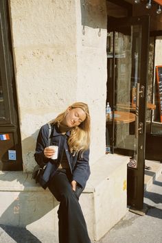 a woman is sitting on the curb with her eyes closed and drinking from a cup