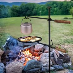 an outdoor grill with food cooking over it in the middle of some rocks and grass