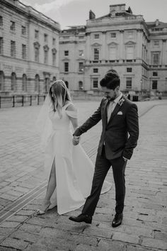 a bride and groom holding hands walking in front of an old building with stone floors