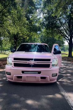 the pink truck is parked on the side of the road in front of some trees