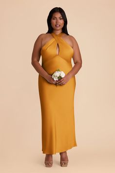 a woman in an orange dress holding a white flower and standing against a beige background