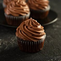 three chocolate cupcakes with frosting on a black plate, close - up