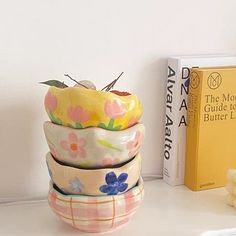 a stack of ceramic bowls sitting on top of a white shelf next to a book