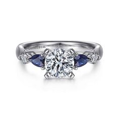 a white gold engagement ring with blue sapphire stones on the sides and an oval diamond center