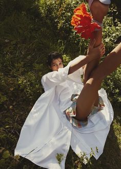 a person laying on the ground with a flower in their hand and wearing a white dress