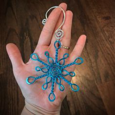 a hand holding a blue string wrapped snowflake ornament in it's palm