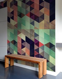 a wooden bench sitting in front of a wall covered in multicolored geometric tiles