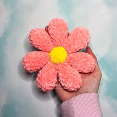 a hand holding a small pink flower with a yellow center