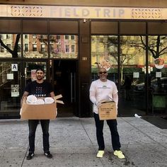 two men holding boxes with donuts on them in front of a large building that says field trip