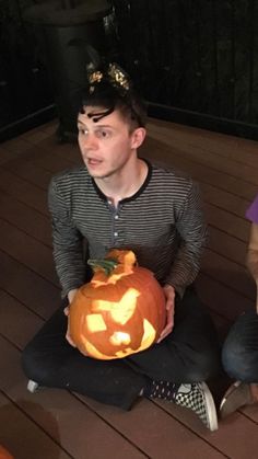 two people sitting on the ground holding a carved pumpkin