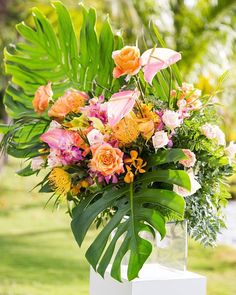 a vase filled with lots of colorful flowers on top of a white table next to a tree