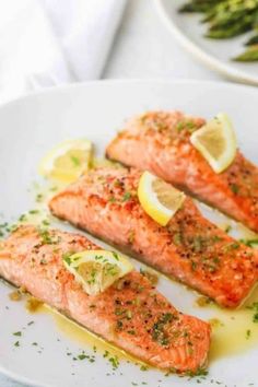 two salmon fillets on a white plate with lemons and parsley garnish