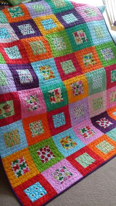 a multicolored patchwork quilt is on the floor in front of a window