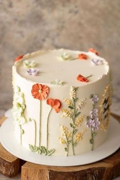 a white cake with flowers on it sitting on top of a wooden sliced board