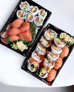 two black trays filled with sushi on top of a white table next to each other