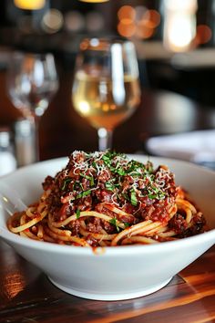 a white bowl filled with spaghetti and sauce on top of a table next to a glass of wine