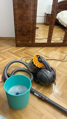 a blue bucket filled with water next to a vacuum cleaner and a yellow flower on the floor