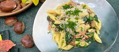 a white plate topped with pasta covered in cheese and vegetables next to autumn leaves on the table