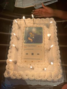 there is a cake with candles on it and someone holding a book in the background