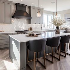 a large kitchen with an island in the middle and four chairs around it, along with two vases filled with flowers