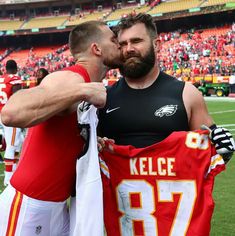 two men standing next to each other in front of a football stadium holding a jersey