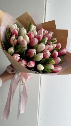 a bouquet of tulips with pink ribbon tied around the ends is held by someone's hand