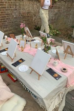 a table with several easels and paintings on it, in front of a brick wall