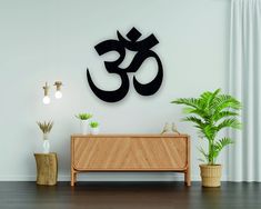 there is a wooden cabinet and potted plant in front of the wall that has an om symbol on it