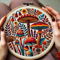 the woman is holding up her embroidery art piece with colorful mushrooms and flowers on it