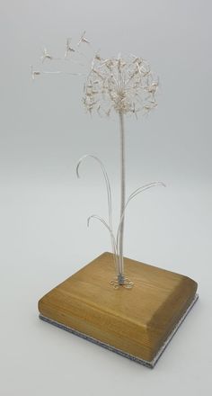 a glass flower on a wooden stand with white flowers in the center and silver stems sticking out of it