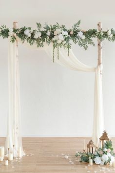 a white wedding arch decorated with greenery and candles