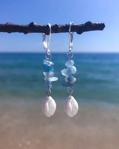 sea glass earrings hanging from a branch in front of the ocean with clear blue water