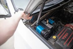 a person is working on an engine in a white car with its hood open and it's battery removed