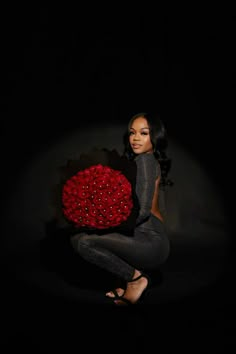 a woman kneeling in the dark holding a large red ball with roses on it's side