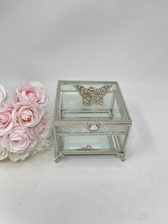 a glass jewelry box next to flowers on a white surface