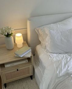 a bed with white sheets and pillows next to a night stand with a book on it