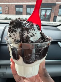 a person holding an ice cream sundae in their hand with a red spoon sticking out of it