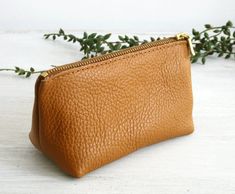 a brown leather pouch sitting on top of a white table next to a plant with green leaves